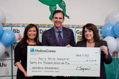 Three people hold a large $25,000 check from MolinaCares for Family Service Association, smiling at the camera.