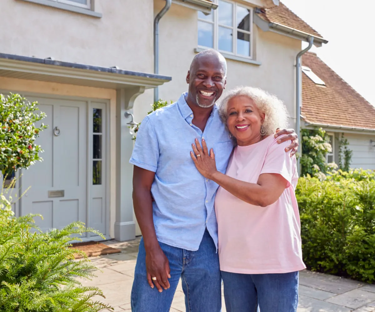 Smiling couple standing together outside their house on a sunny day.