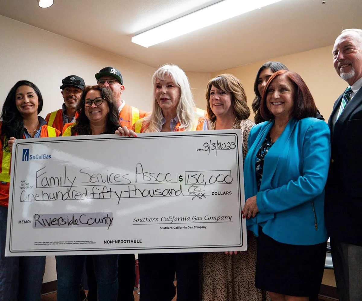 A group of people smiles holding a $150,000 check made out to Family Services Assoc. from SoCalGas.