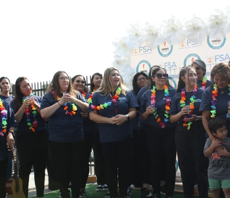 A group of women in navy shirts and colorful leis stand together, smiling at an outdoor event.